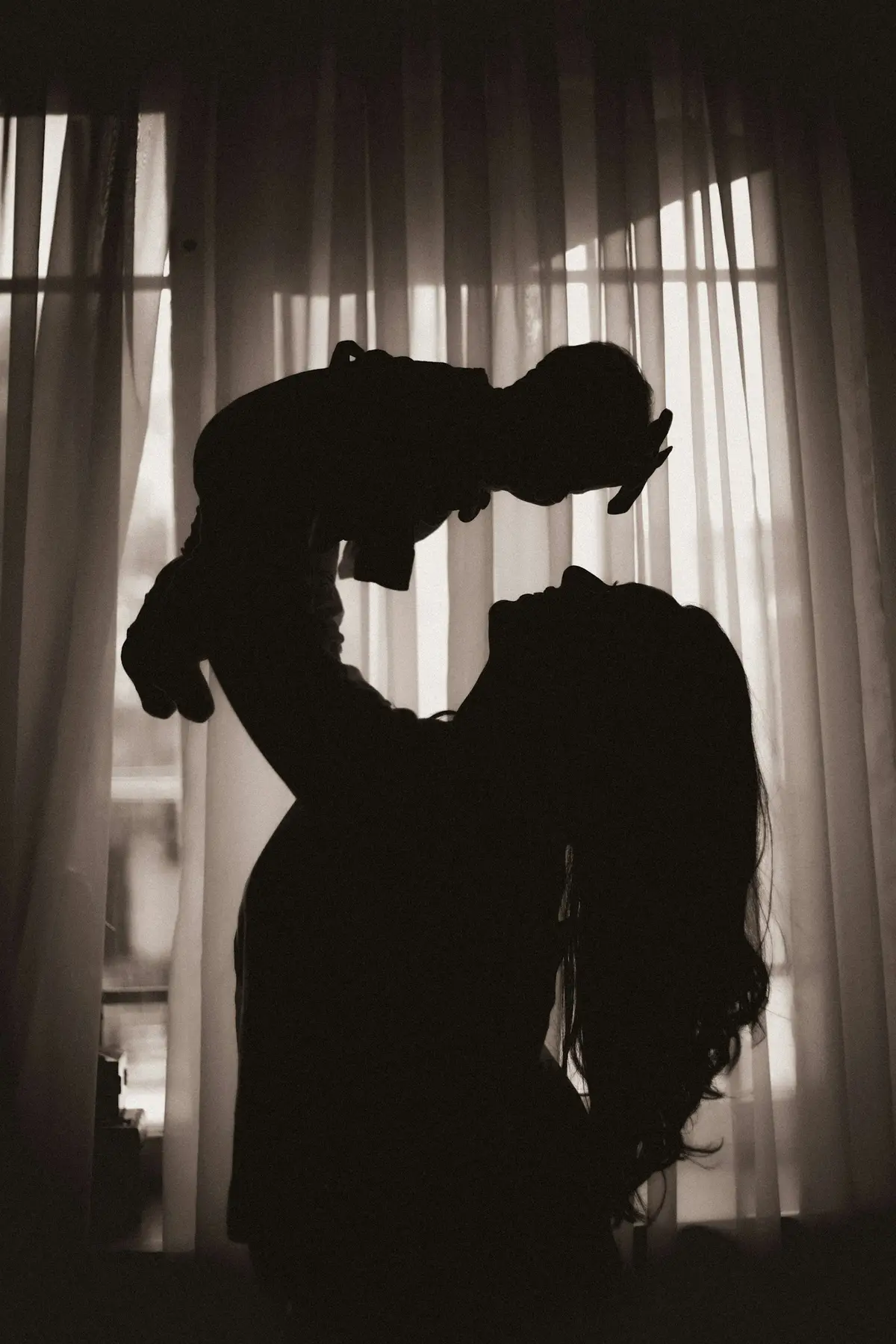Silhouette of a mother lifting her baby in front of a window.