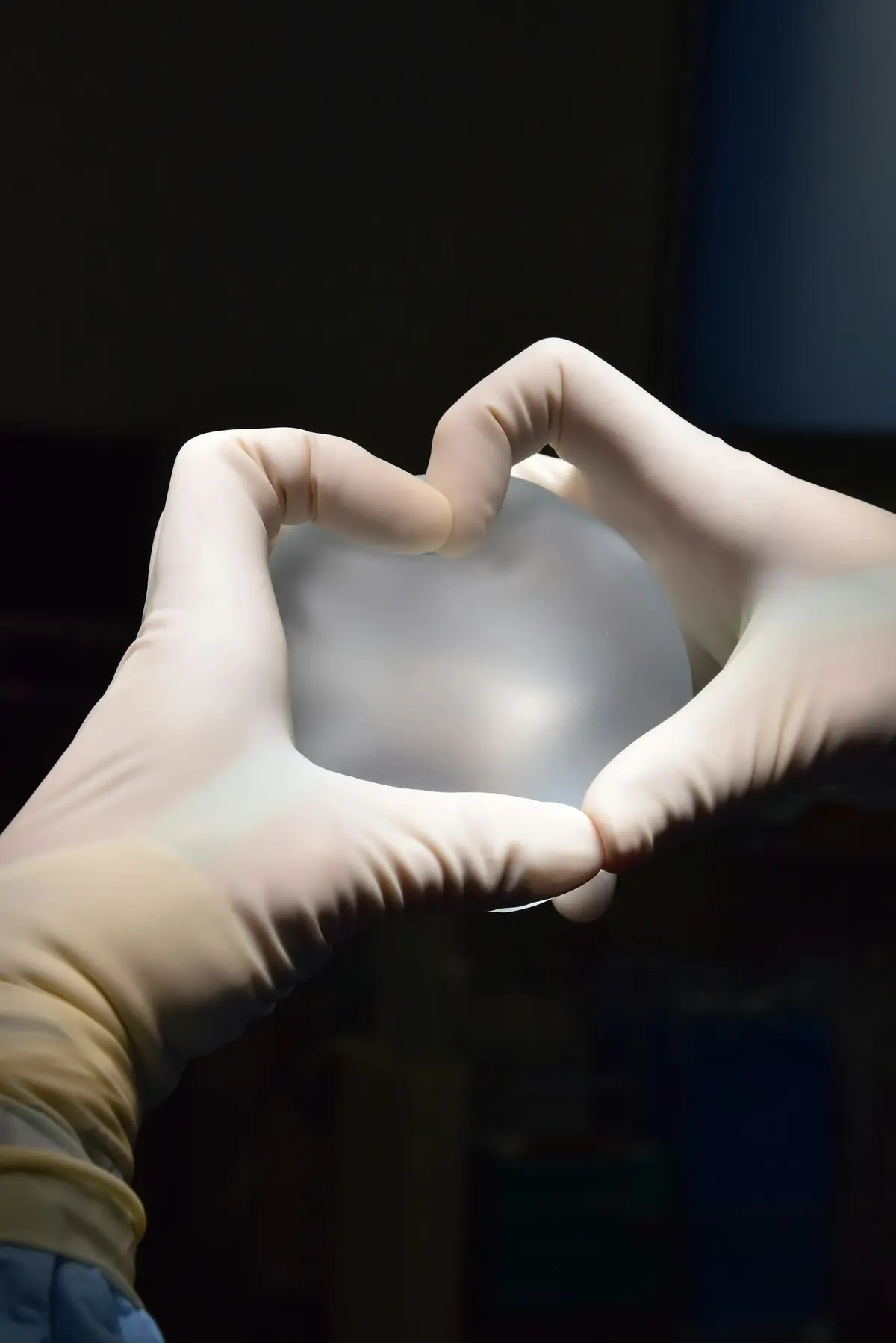 Unas manos enguantadas sostienen un implante mamario de silicona.