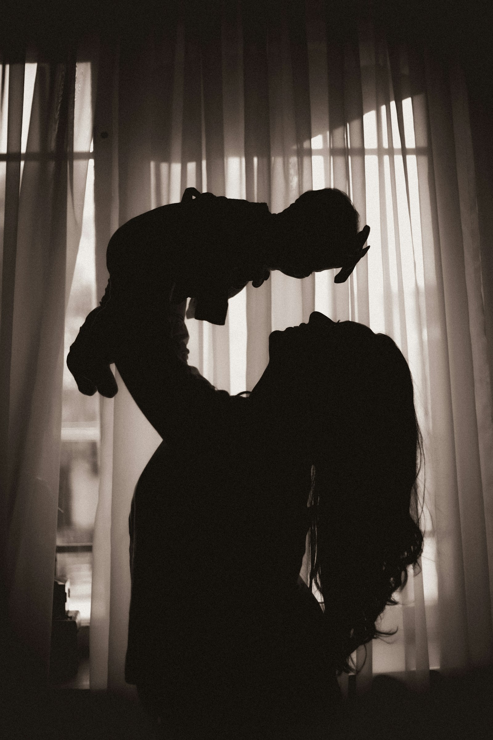 Silhouette d'une mère soulevant son bébé devant une fenêtre